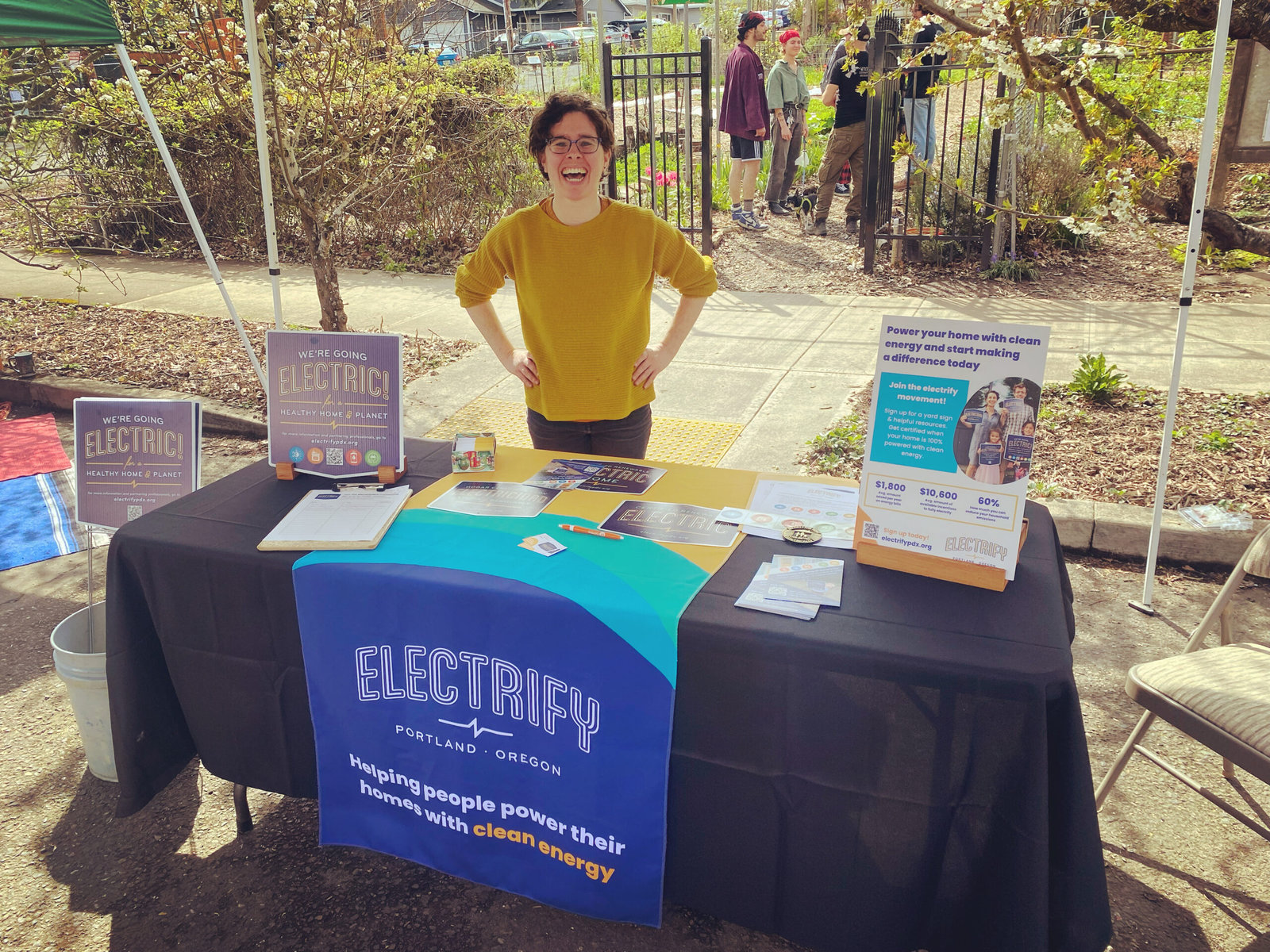 A woman stands behind ElectrifyPDX's table at an Earth Day fair.