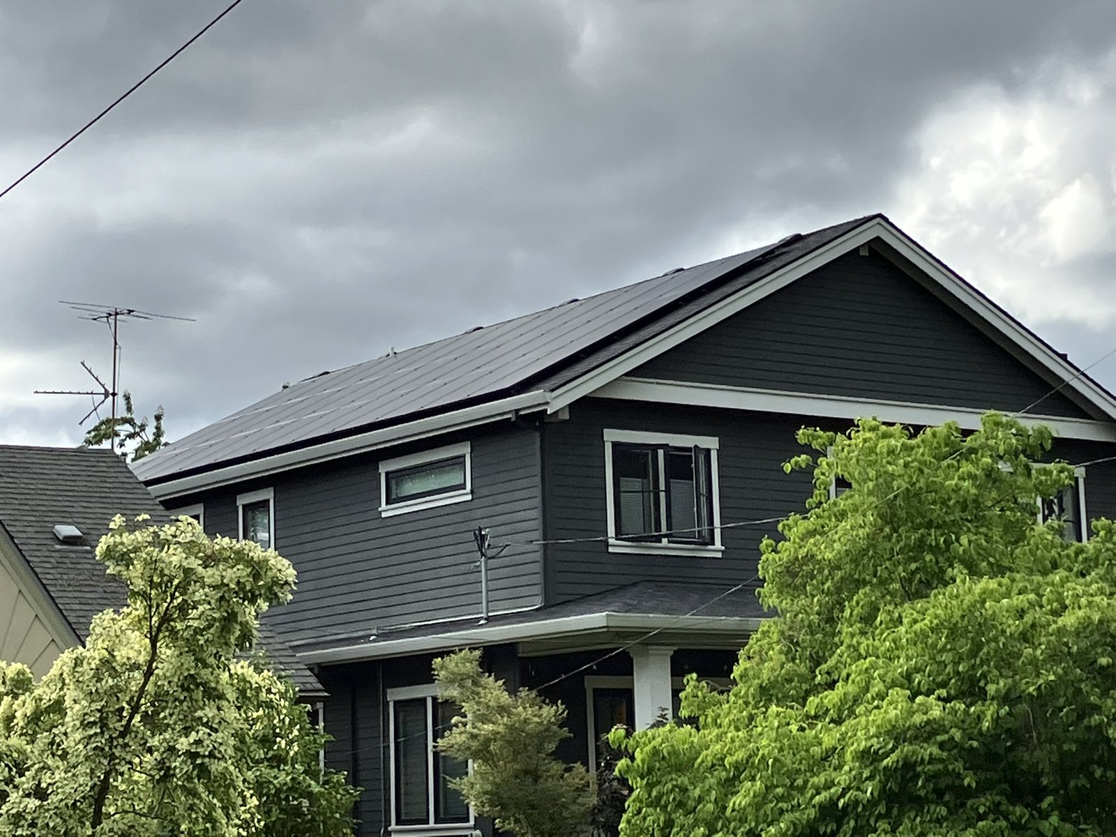 A grey house with solar panels on the roof under cloudy skies.