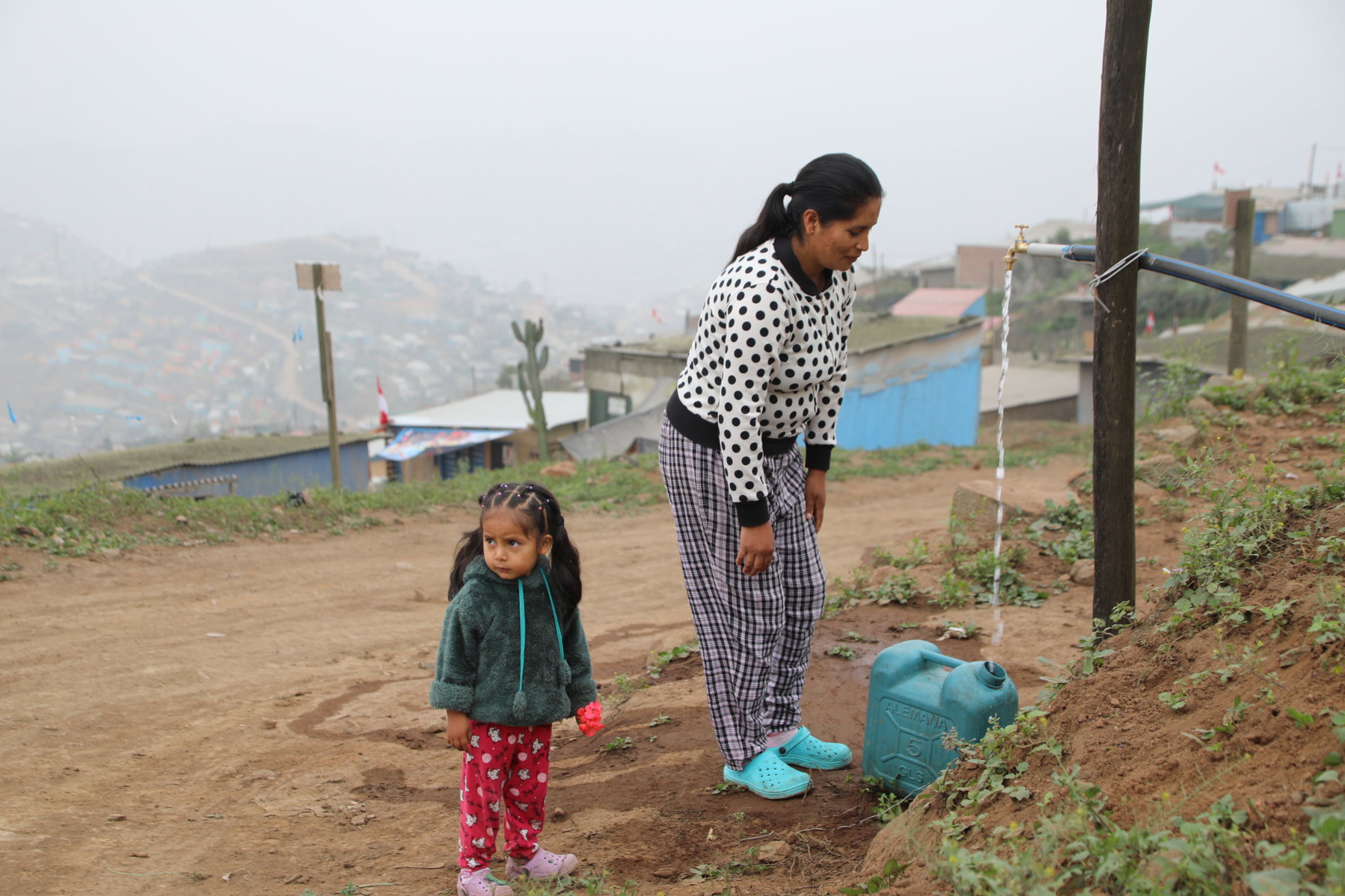 Isabel Quispe and Gabriel Jaio's niece Vilma and her daughter fill a plastic container with water from a tap.