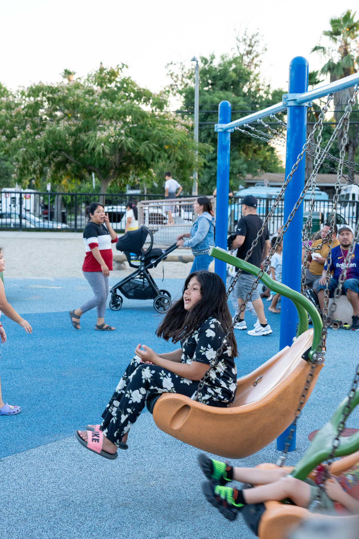 Residents play on a coated playground. A young girl is swinging on a swing in the foreground.