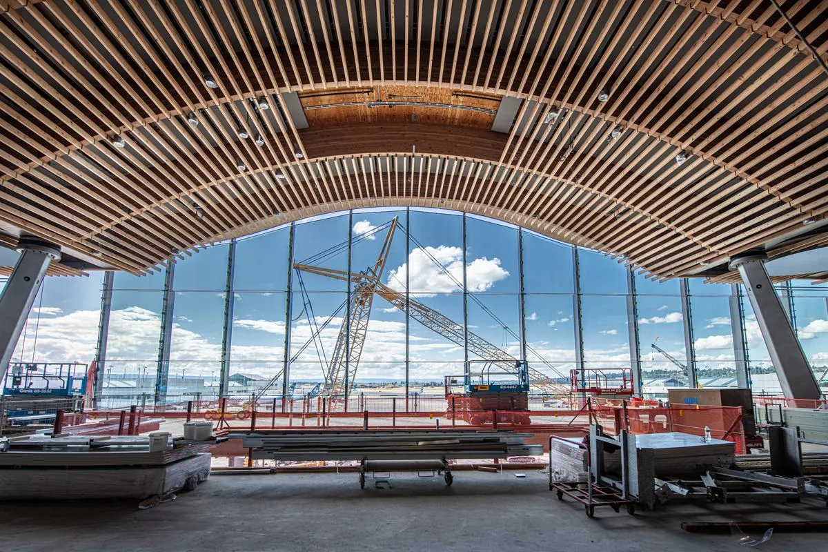 Timber roof at Portland airport while under construction. Cranes are visible out the huge windows.