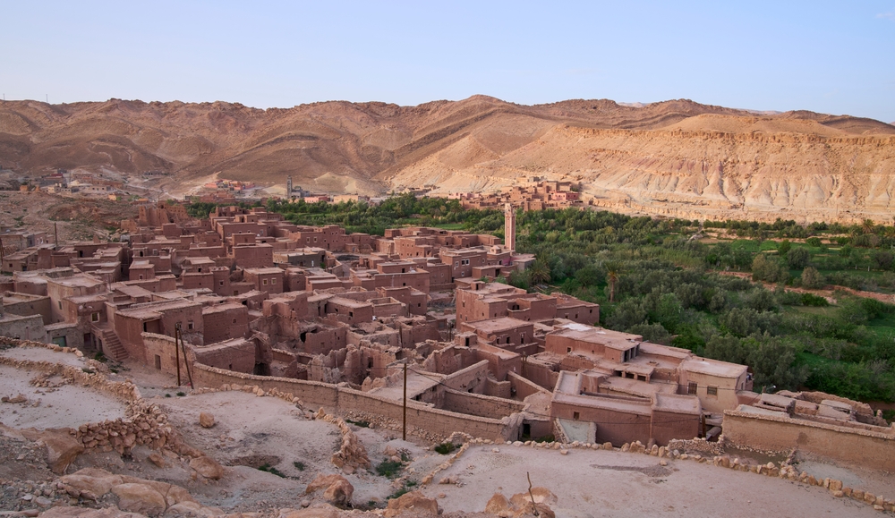 A village built of stone the same reddish color of the mountains behind it in Morocco.