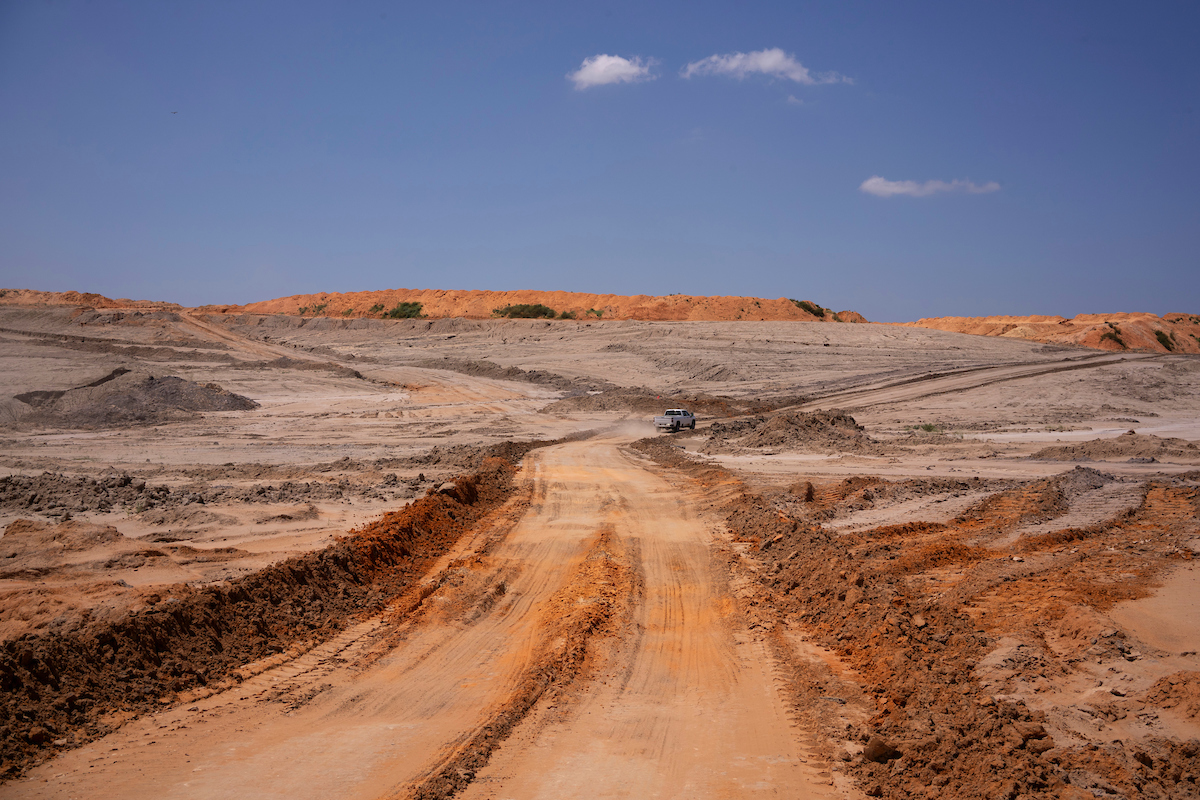 A truck drives away from a dragline excavator and across a dirt road that winds between layers of sediment in a section of the NRG Jewett Mine that is undergoing environmental reclamation. 