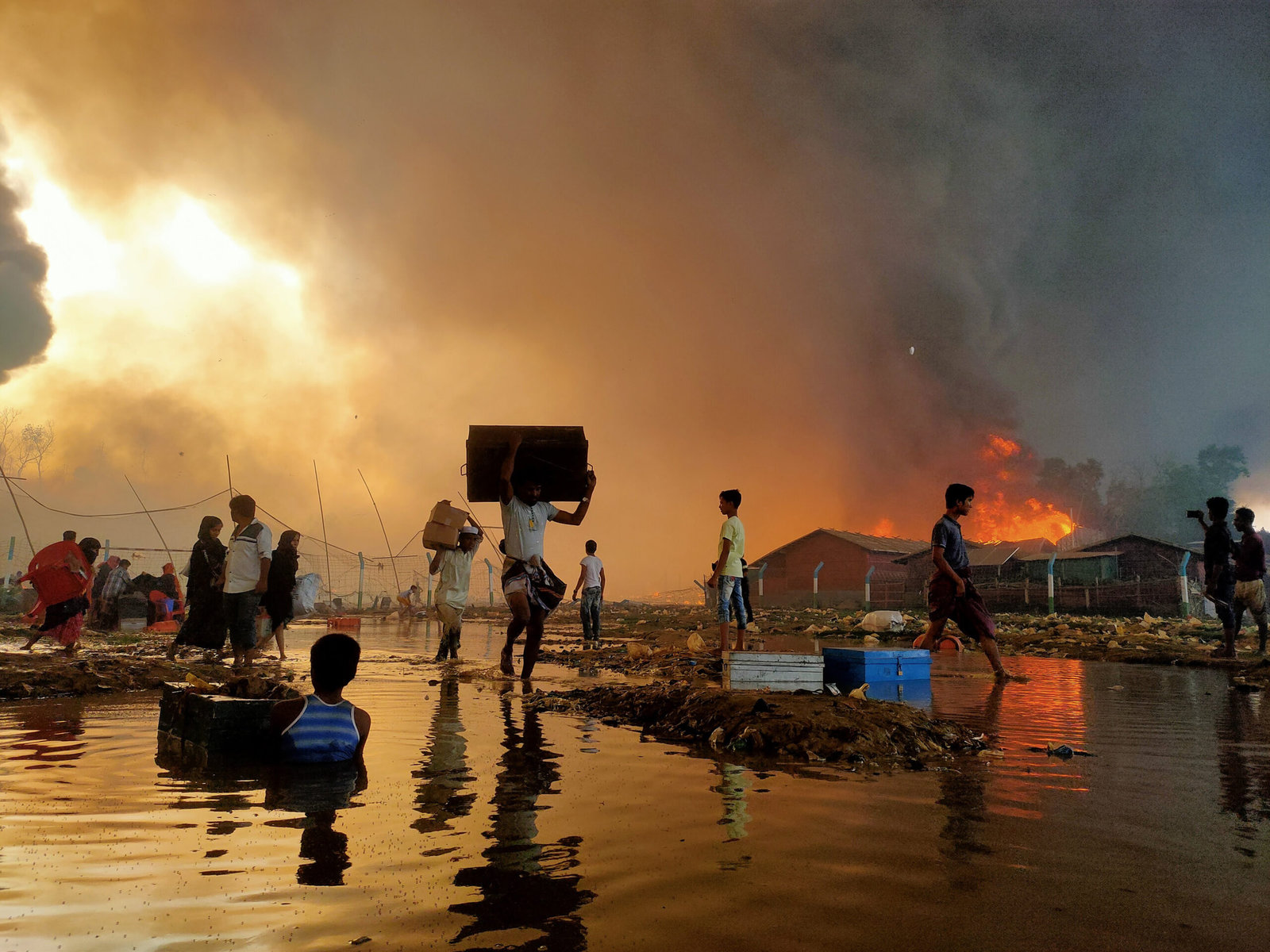 People rush to save their lives and property from a big fire in Balukhali camp. The fire is visible in the background.