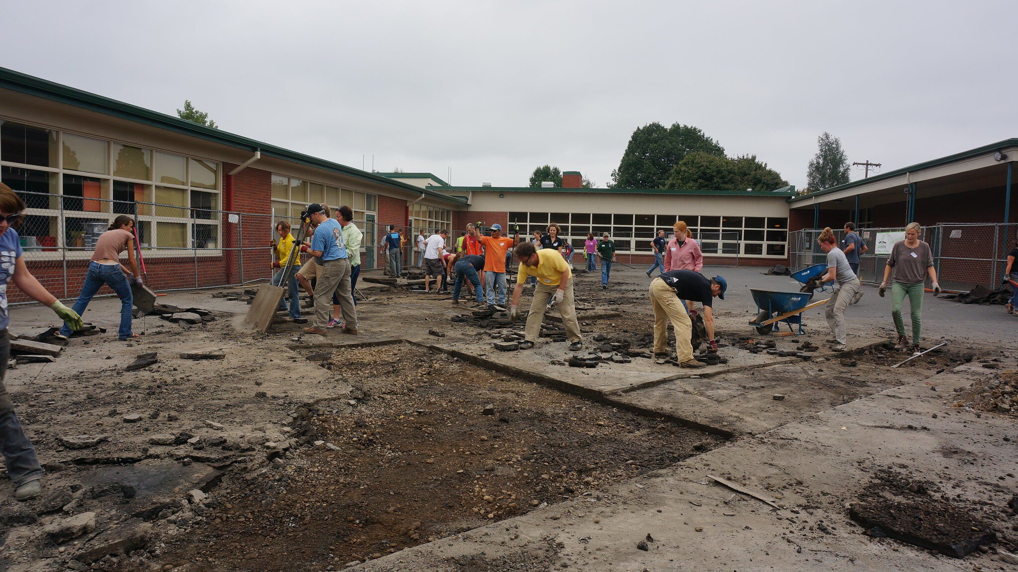 A group of volunteers are ripping out pavement outside a school.