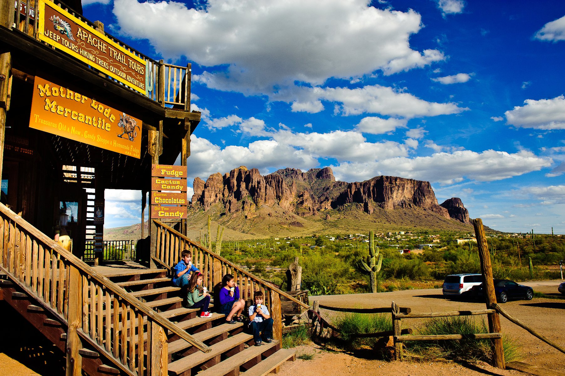 A family sits on the steps of a shop in an Arizona "ghost town" with saguaros and red rocks in the background.