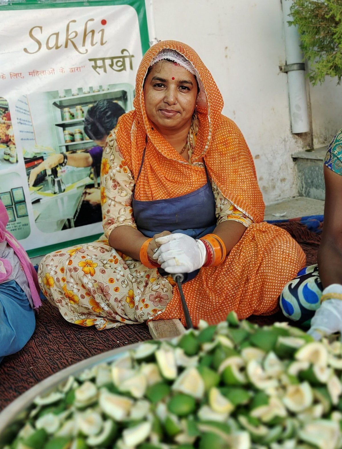 A woman sits with a bowl of fruit in front of her.