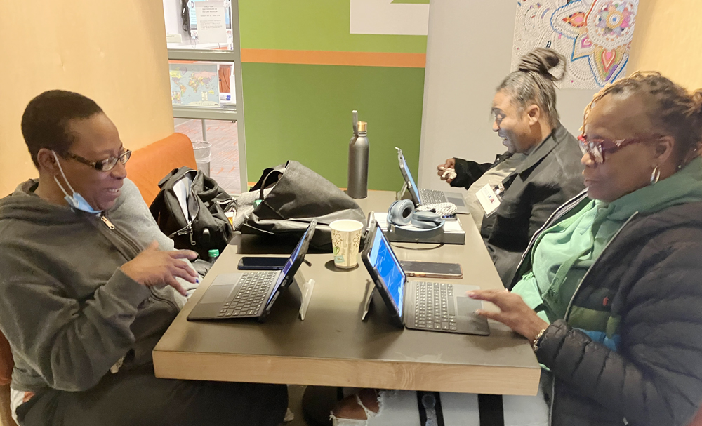 Students Joyce Neal, 52, Carla Thompson, 41, and Rhonda Jones, 55, talk as they study for a standardized math test. They sit at a table with laptops in front of them.