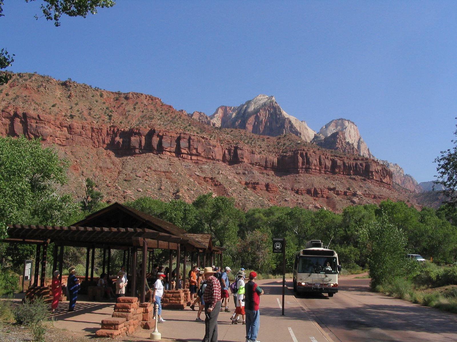 A shuttle bus waits outside the visitor center at Zion National Park, with red rock formations in the background.