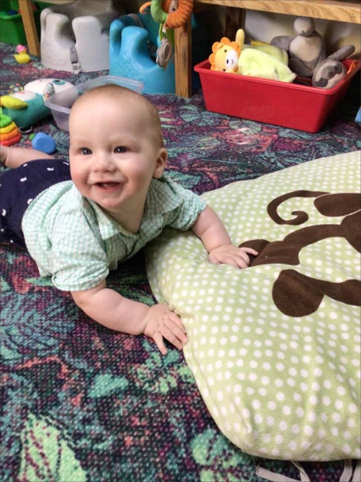 A baby lying on his belly and smiling.