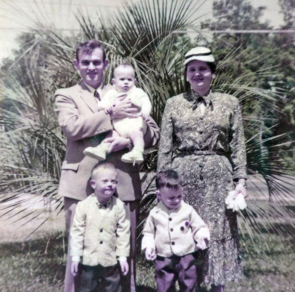 An old photo of a family at a christening with tropical plants behind them.