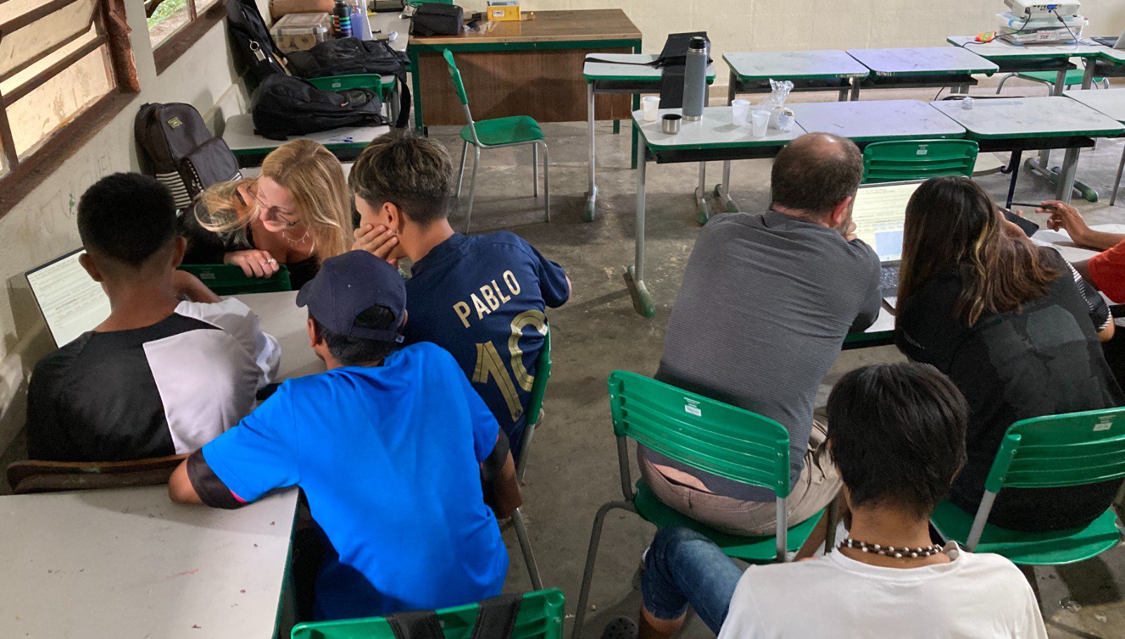 Students gather around laptops to learn language skills from an app.