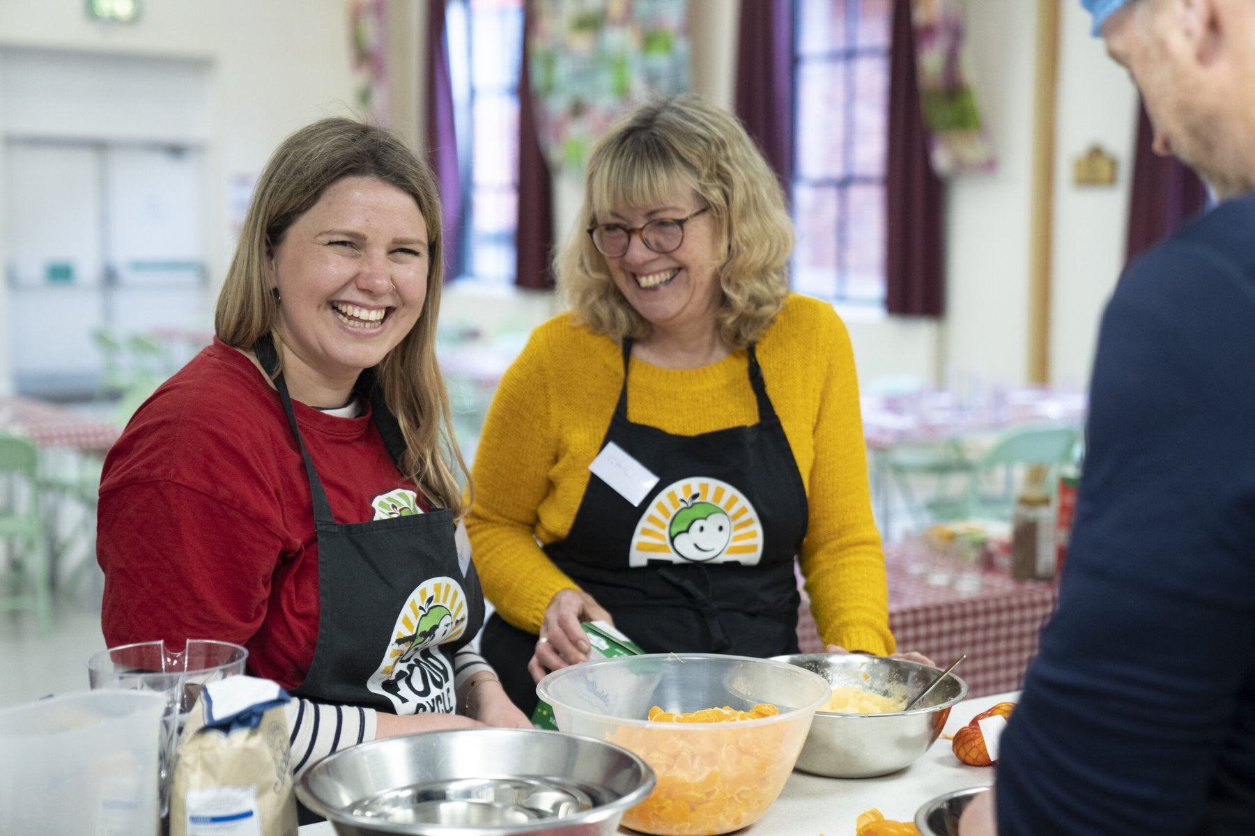 Two women in aprons are smiling as they prepare a custard.