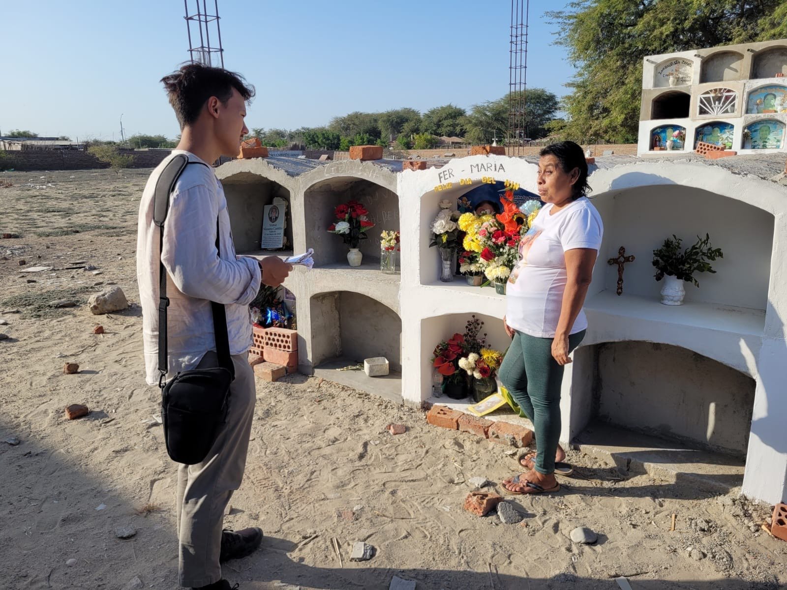 Journalist Peter Yeung talks with a woman in front of a memorial for people who have died from dengue fever in Peru.