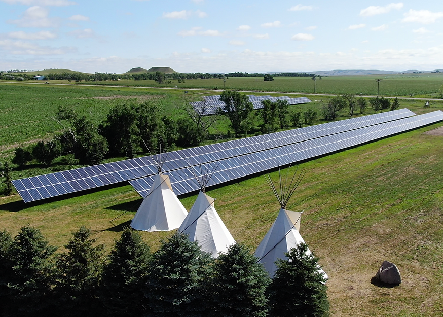 Teepees stand in front of solar panels in a green field.