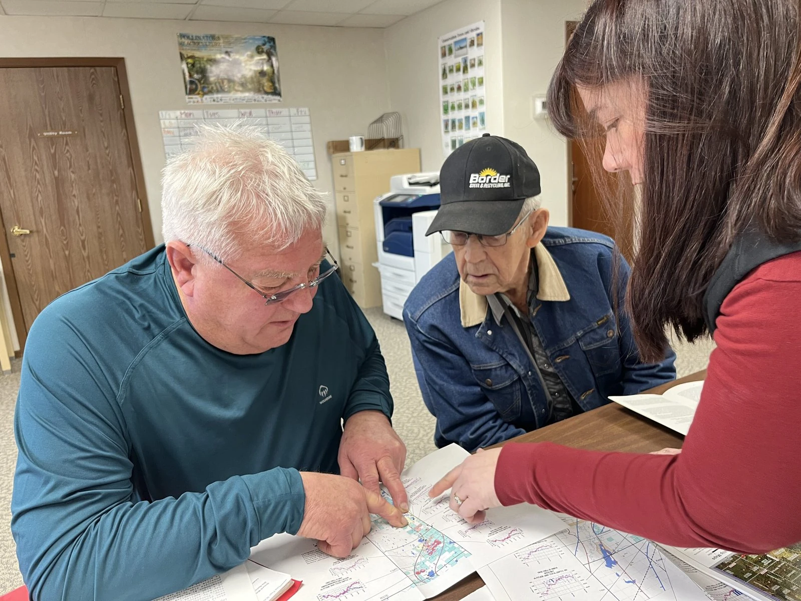 From left to right, Jeff Wivholm, Marlowe Onstead and Amy Yoder look through maps of irrigation pivots and aquifer allocations inside the Sheridan County Conservation District office in Plentywood, Montana.