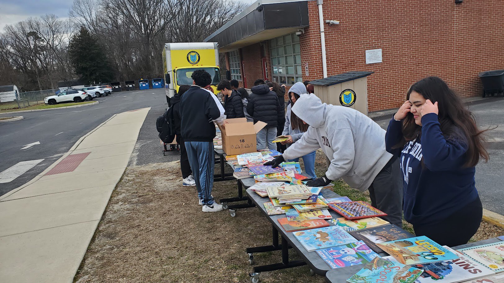 People stand behind tables displaying books outside a brick building.