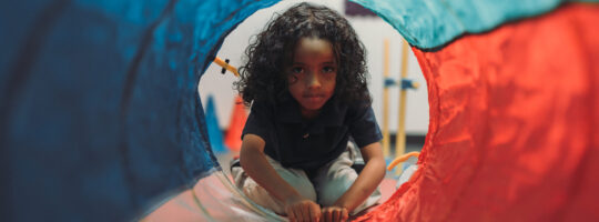 A young girl playing in a toy tunnel.