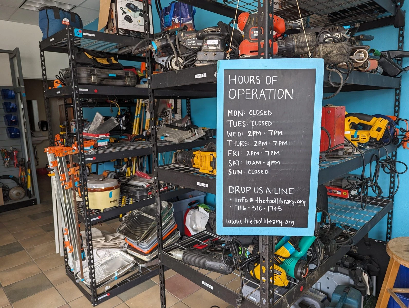 Tools on display at The Tool Library with a chalkboard showing hours of operation.