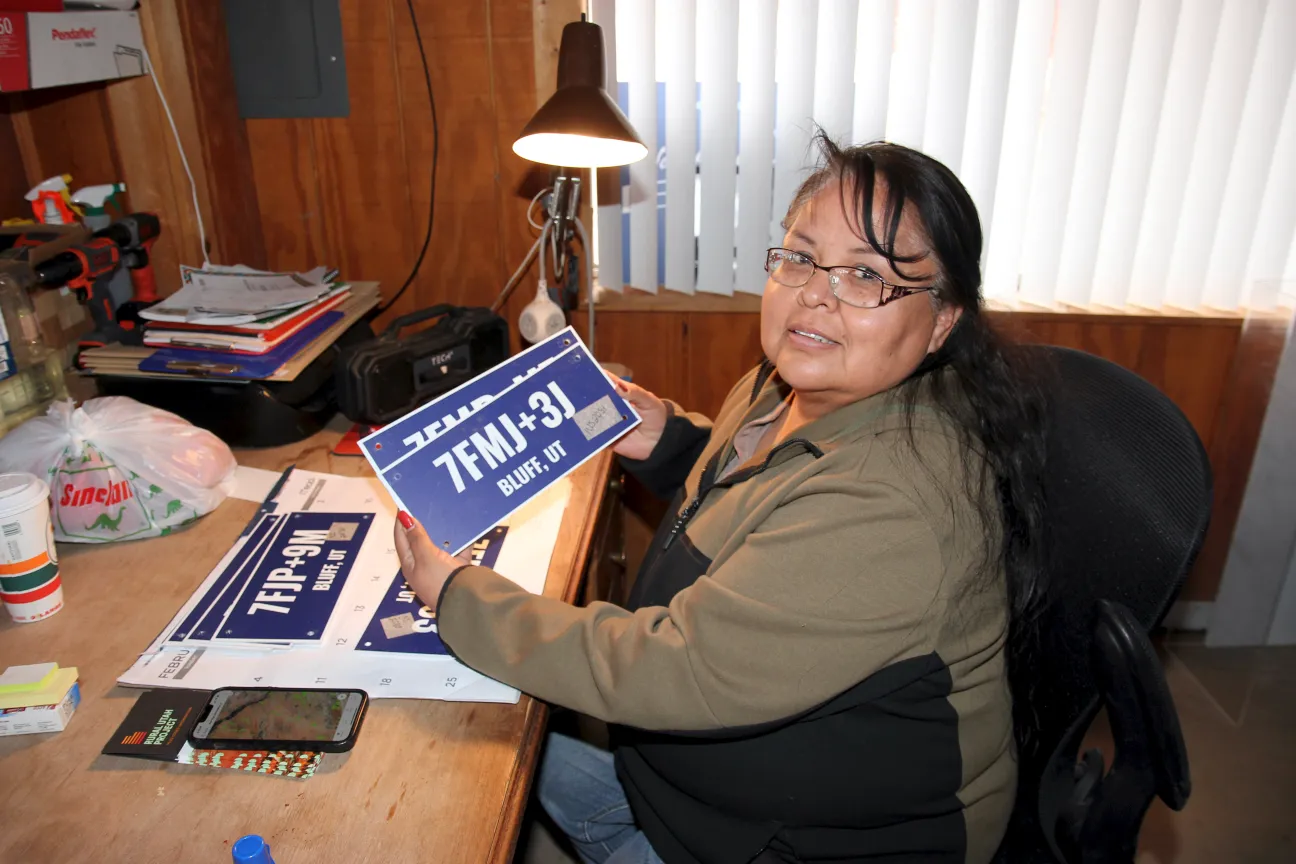 Daylene Redhorse holds up Plus Code signs at her desk.