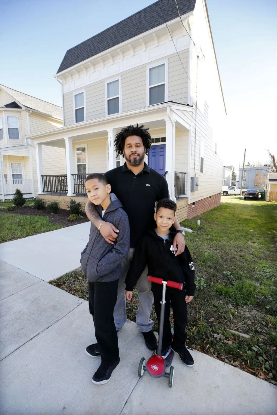 An owner of one of the land trust's homes poses in front of a home with two kids.