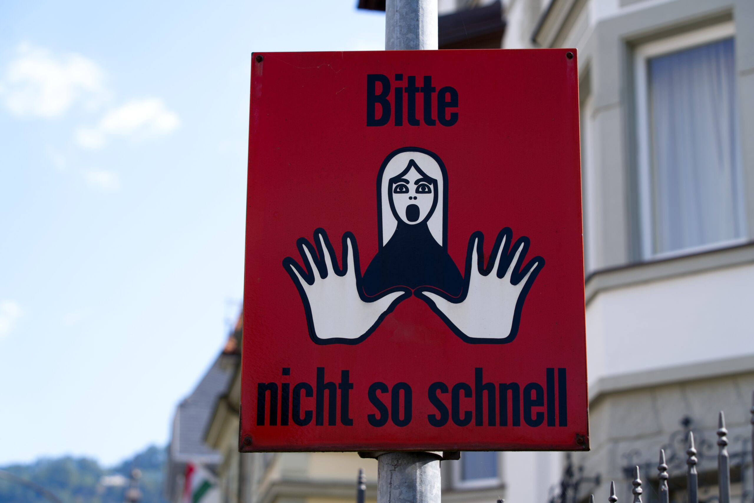 Traffic sign with illustration of a woman and text please not so fast at City of Bregenz on a sunny summer Sunday. 