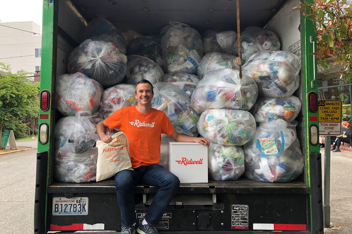 Ridwell co-founder Ryan Metzger sits on the back of a truck full of recycling bags.