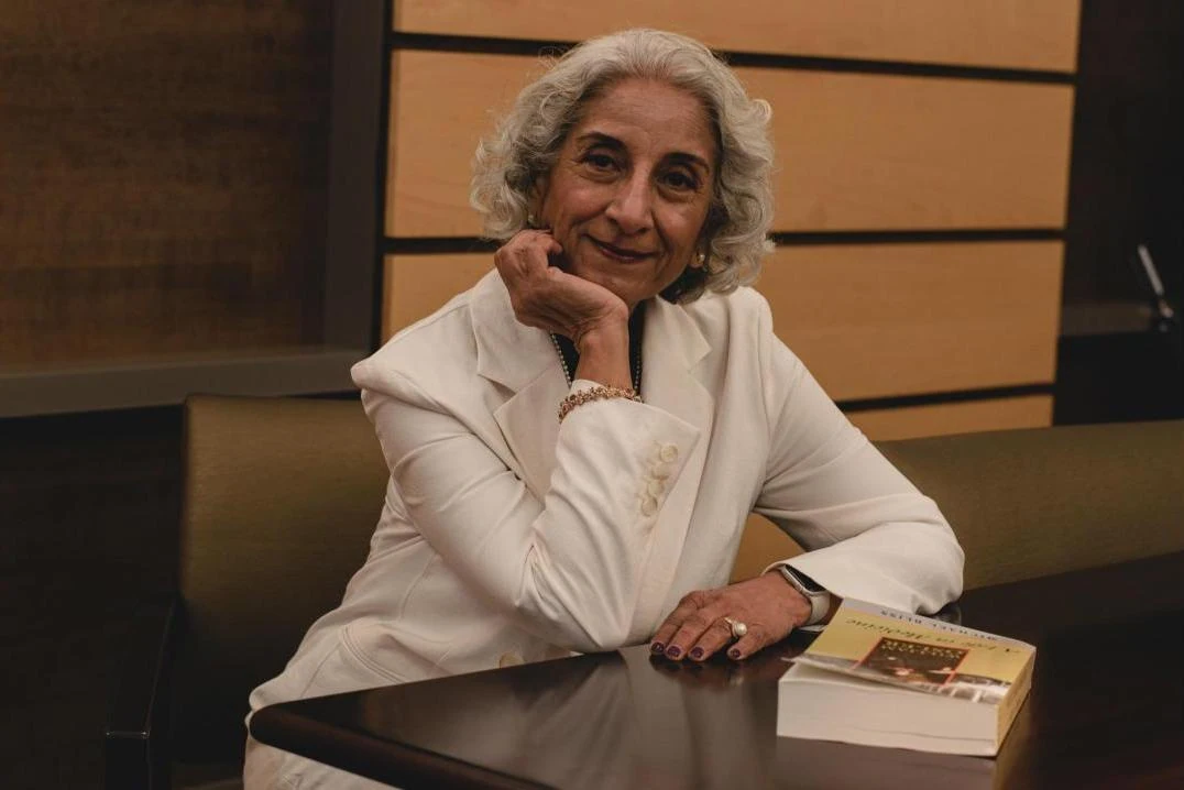 Geetha Jayaram sits at a table wearing a white suit.