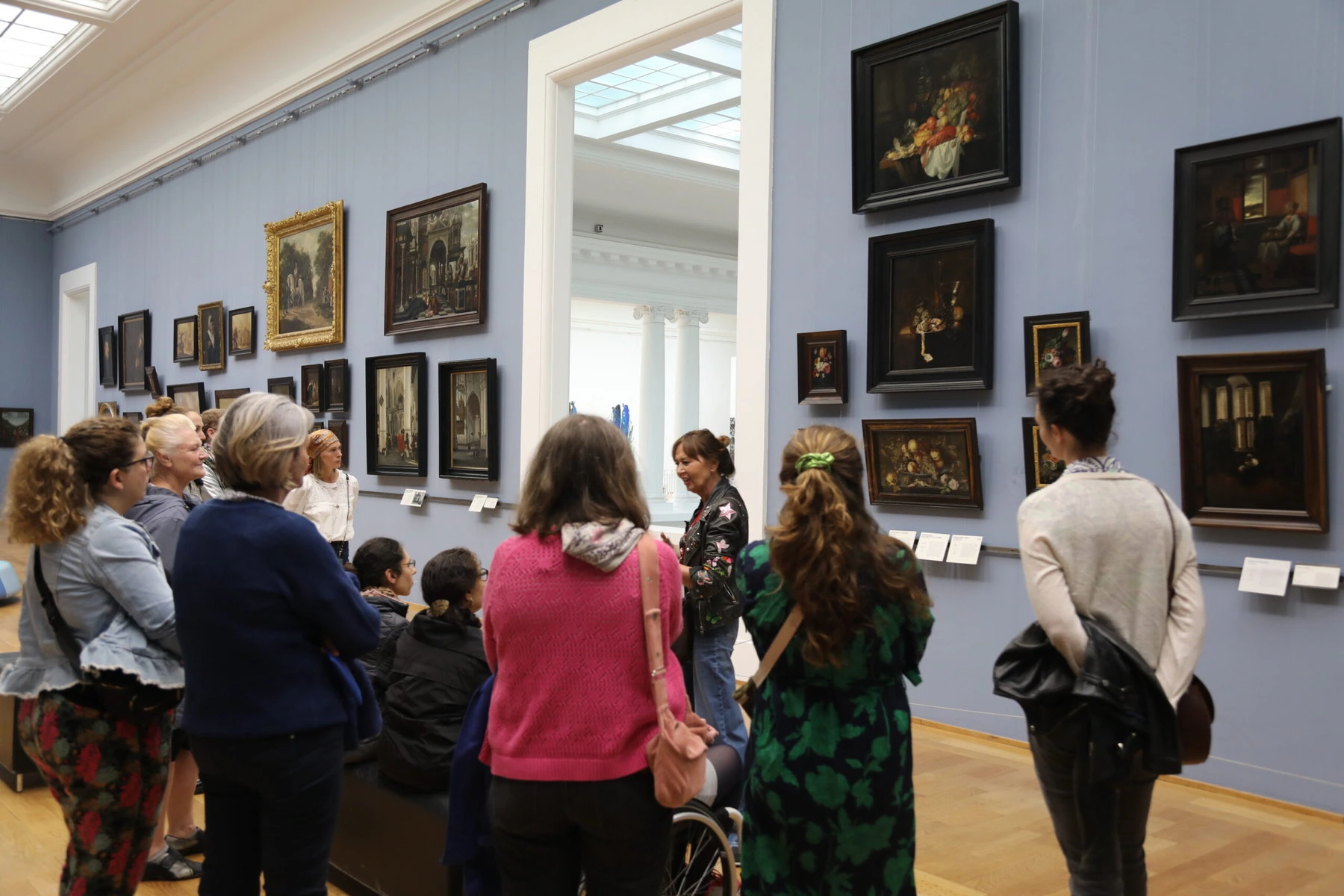 Pascaline Bonnave talking to participants in the Palais des Beaux-Arts in Lille. They are gathered around a wall full of dark-colored paintings.