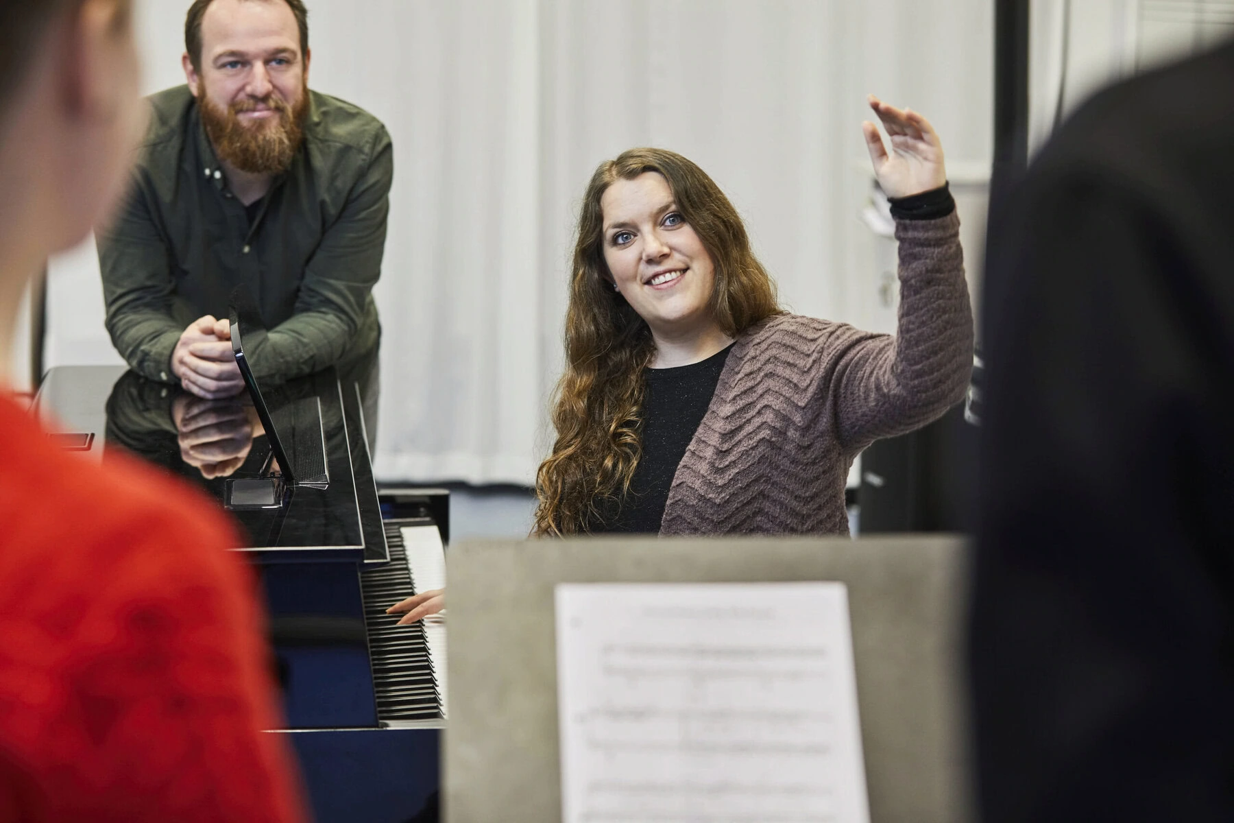 A woman plays piano while directing a choir.