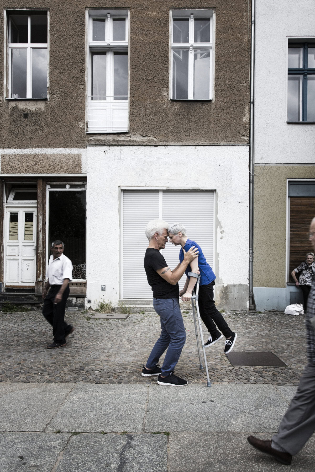 ON A COBBLESTONE STREET IN DAYLIGHT, CUNNINGHAM BALANCES MID-AIR SUPPORTED BY 2 CRUTCHES AND CURTIS’ FOREHEAD. (PHOTO: SVEN HAGOLANI)