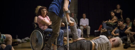 INFORMAL PERFORMANCE SPACE. CURTIS LIES ON WOOD FLOOR AMID CLUSTERS OF AUDIENCE. CUNNINGHAM (ABOVE) PLACES FOOT ON HIS HIP. (PHOTO: SVEN HAGOLANI)