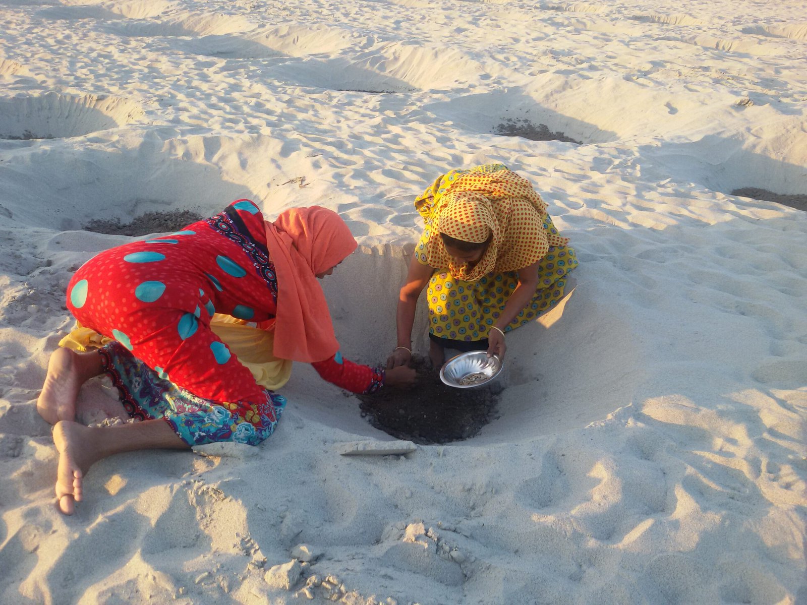 Two women planting seeds in the sand together.