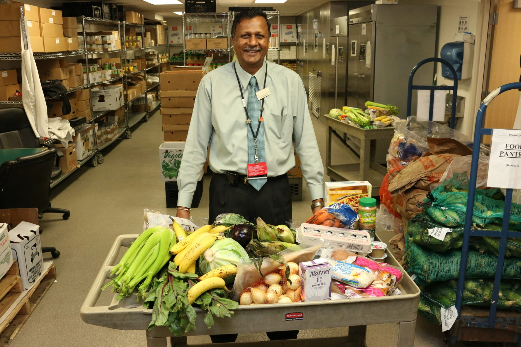 Latchman Hiralall, pantry manager, stands smiling behind a cart full of food.