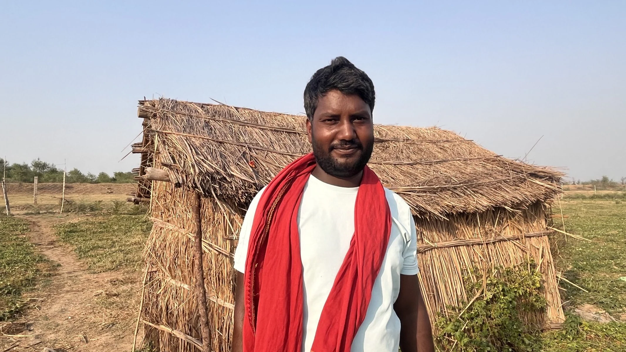 Rohit Bhardwaj stands in front of a shelter. He is wearing a white shirt and red scarf.