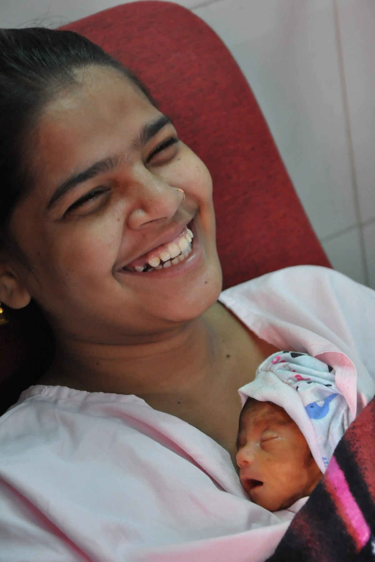 A woman holds her newborn to her chest. She is smiling and the newborn is sleeping.