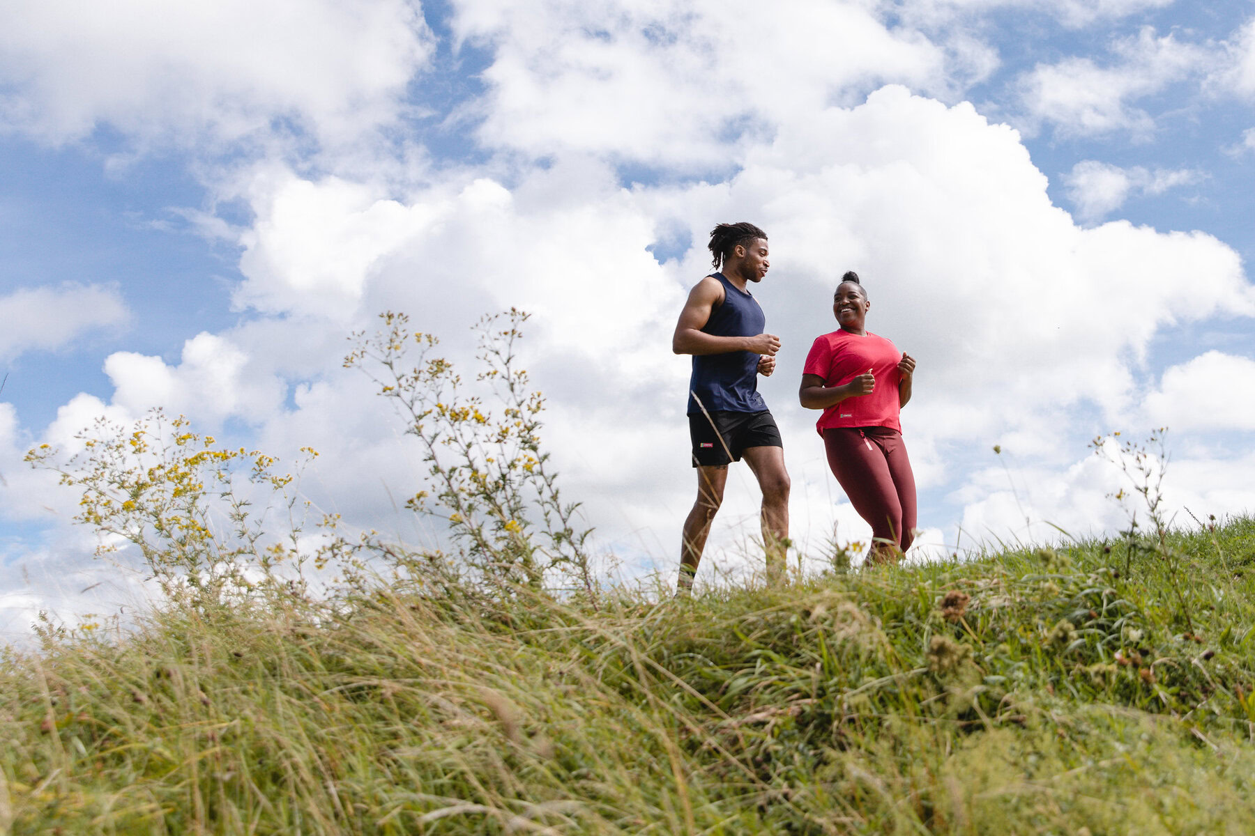 Two people jogging on a grassy hill.