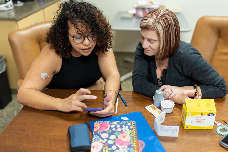 A peer support coach shows a patient how to track her blood glucose levels using an app.