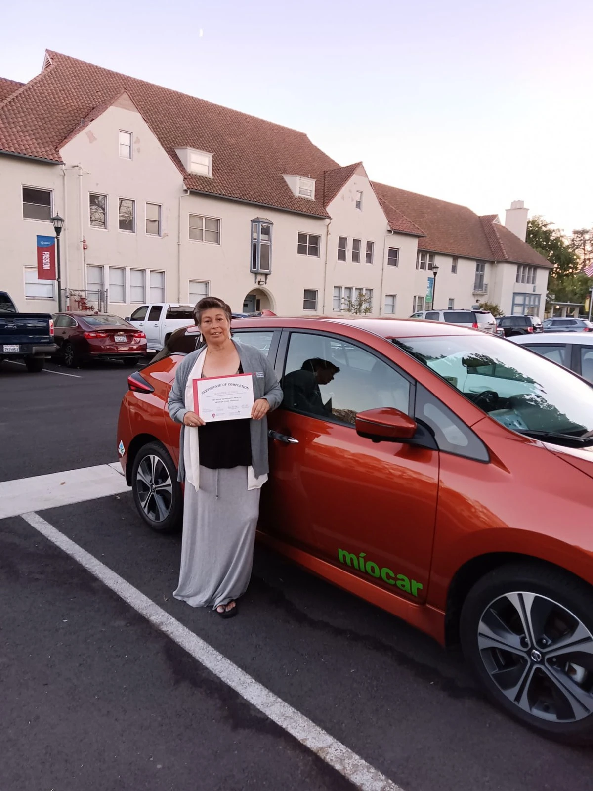 Jennifer Flores poses with a certificate in her hands in front of a red car.