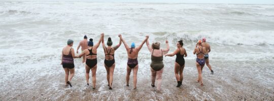 A group of people walk into the ocean for a swim. They are holding hands.