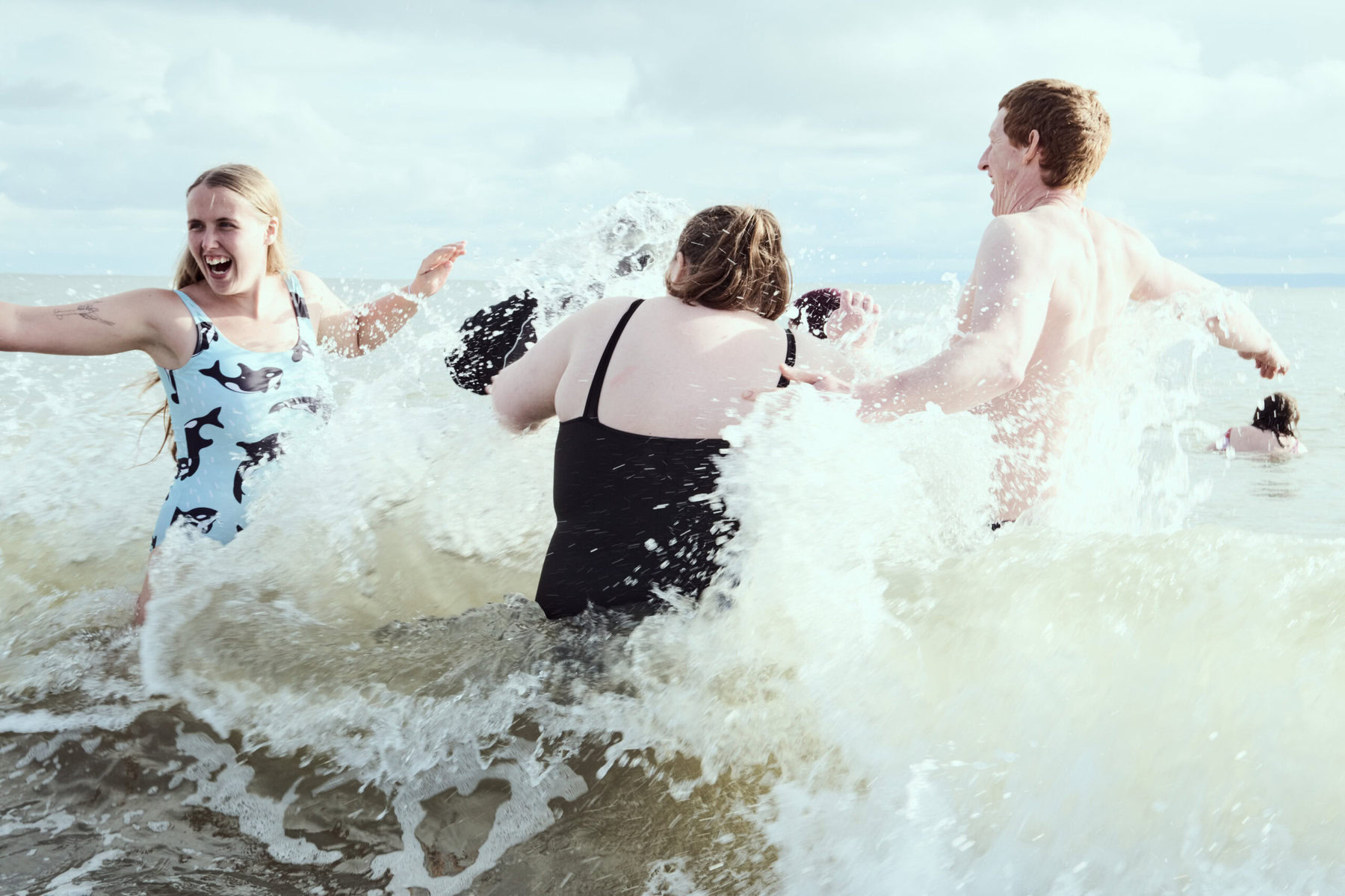 Three people swimming happily and getting splashed by a wave.