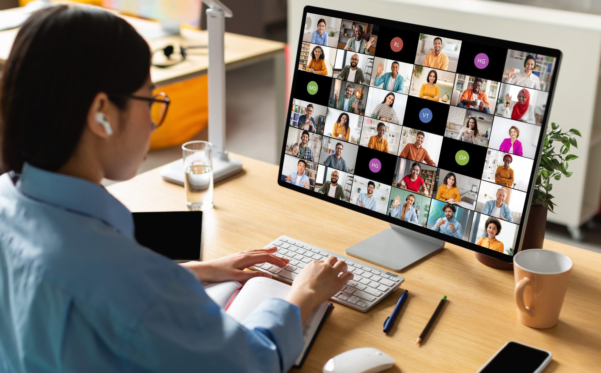 A woman sits in front of a computer on a video call with many participants.