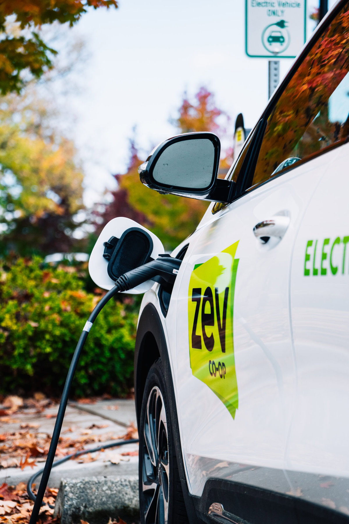 An electric vehicle with "ZEV" written on it is plugged into a charger.