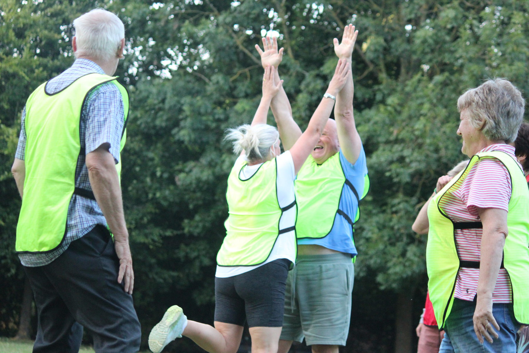 Two people high-five after playing football while others look on. All are wearing neon vests.