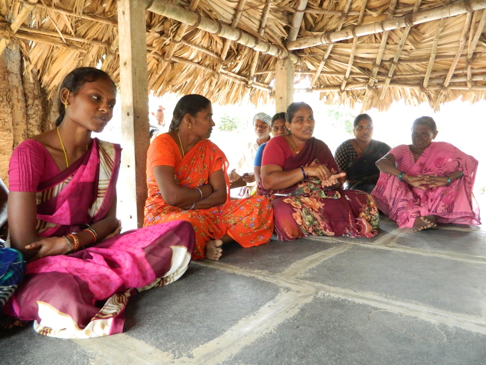 A group of women sit cross-legged wearing pink and orange outfits.