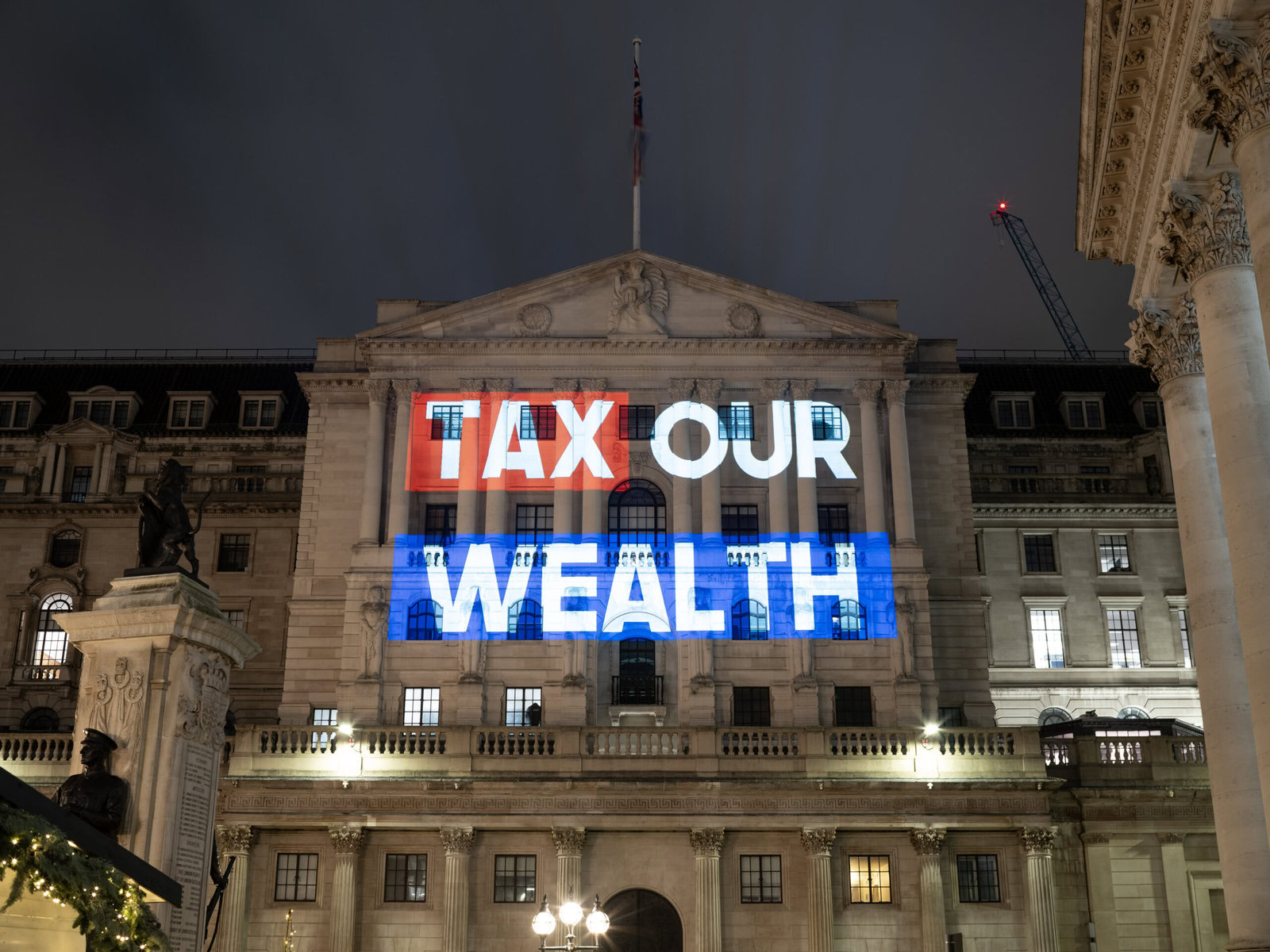 A sign reading "Tax Our Wealth" is projected onto a government building.