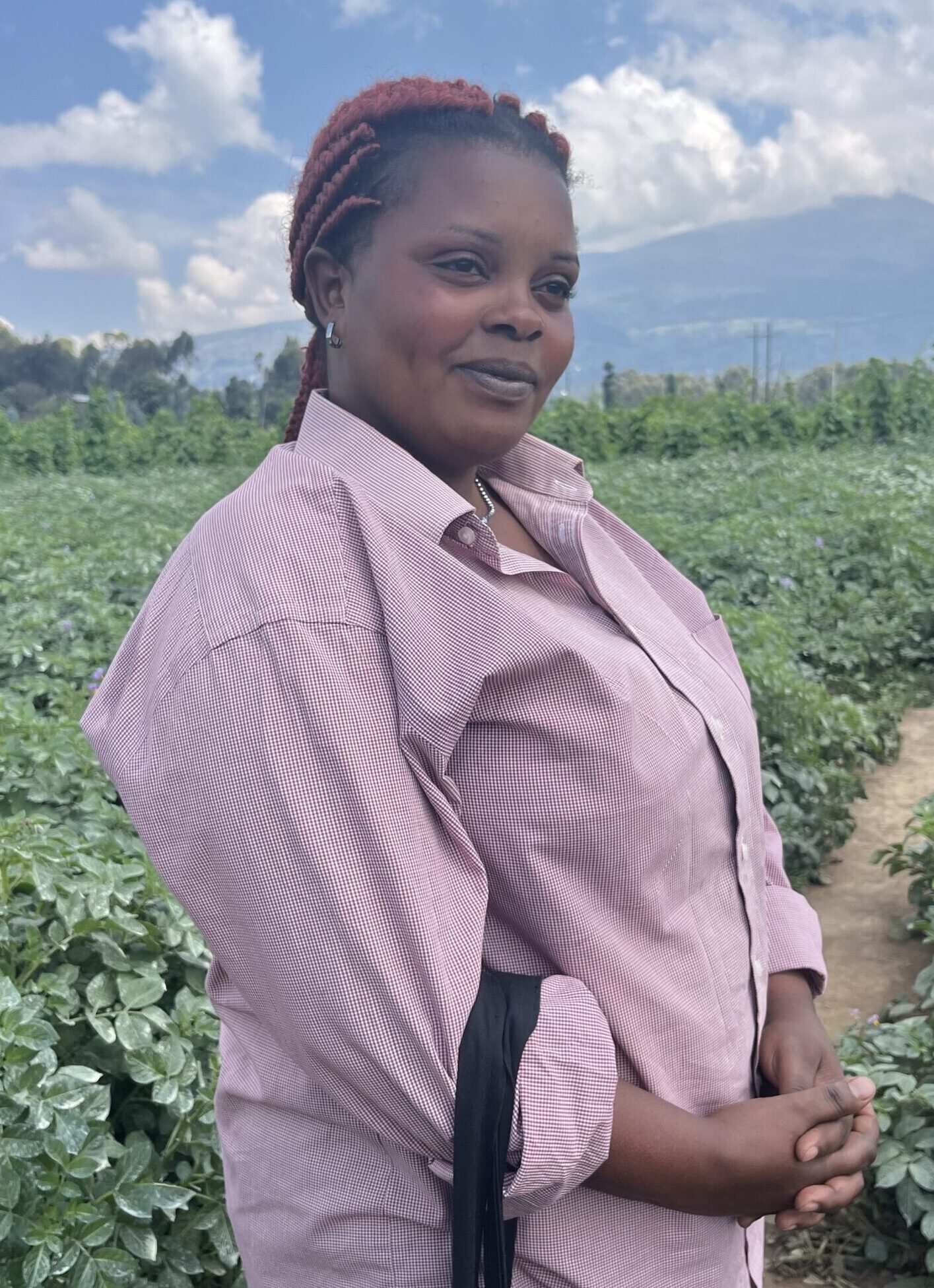 Esperance Dushakimana, potato farmer in Musanze, North Rwanda, stands in a field with crops behind her.