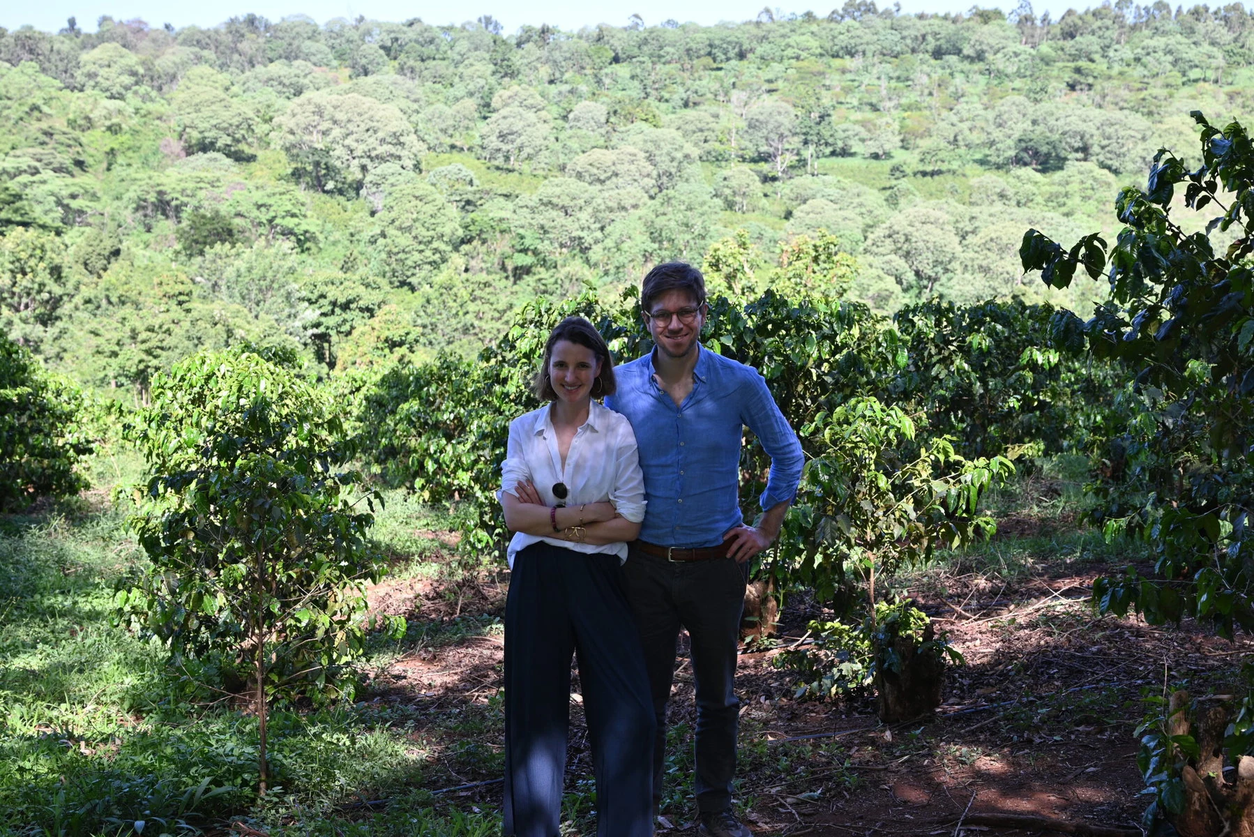 Sophie von Loeben and her partner, Timothy Charlton, pose in front of coffee plants in a forest.