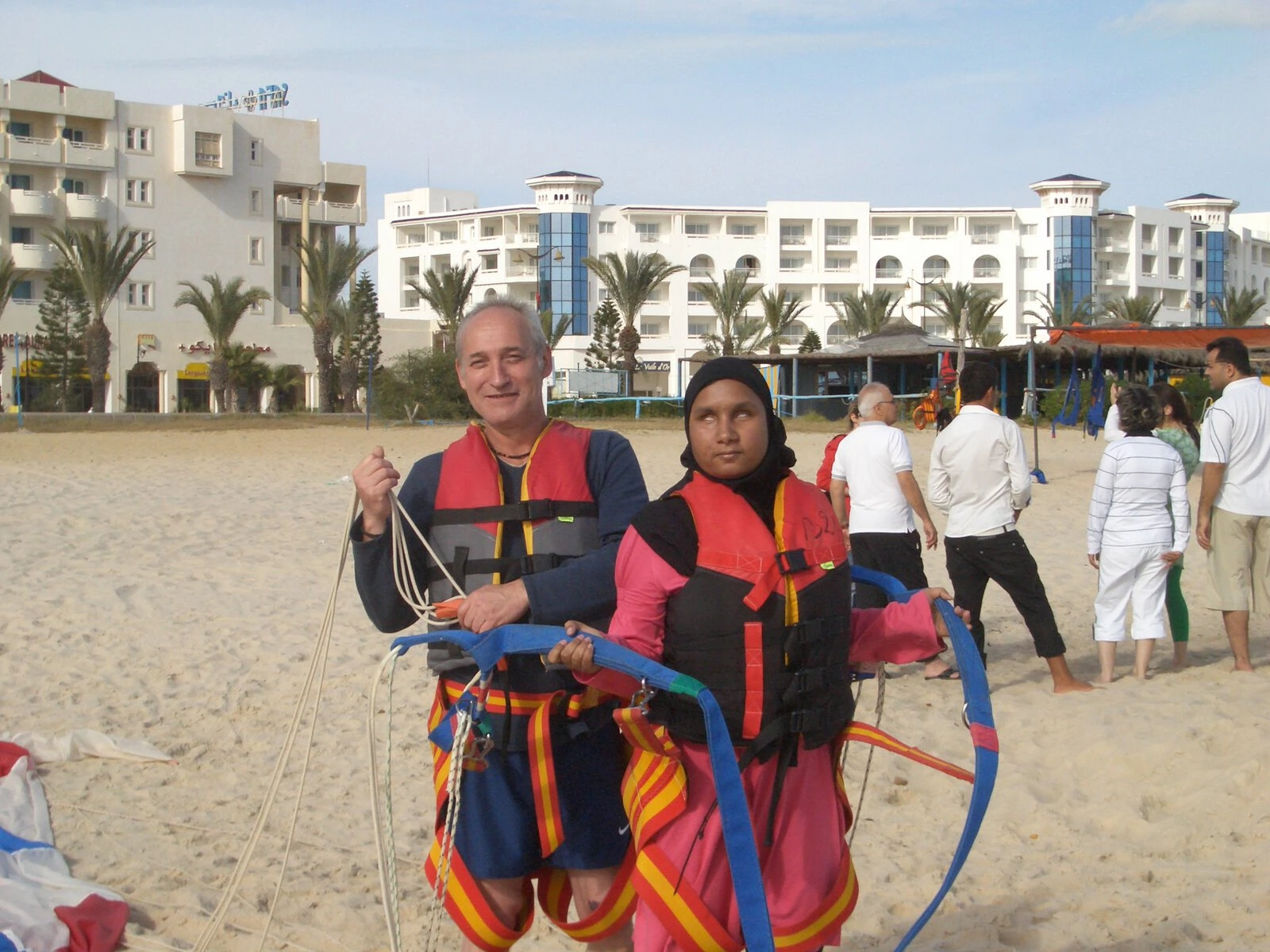 Two people post on a beach, preparing to paraglide.