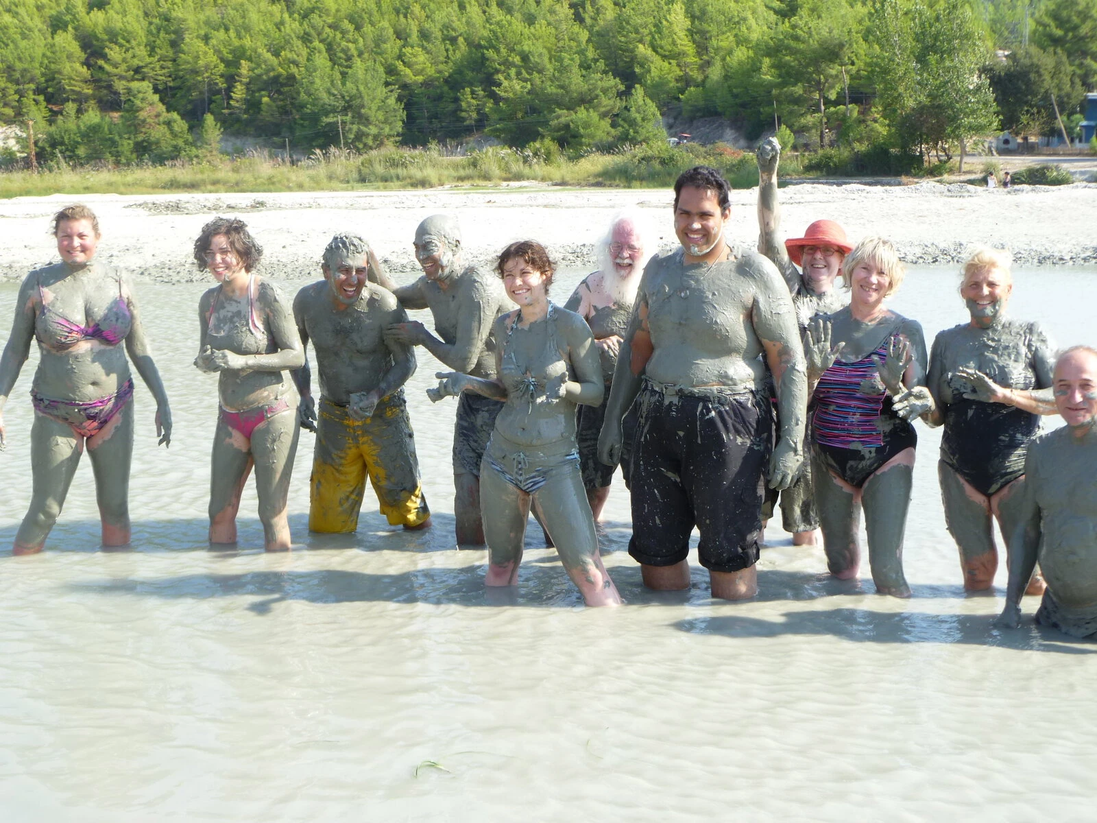 A Traveleyes group in Turkey is standing in murky water. Everyone has covered themselves with mud.